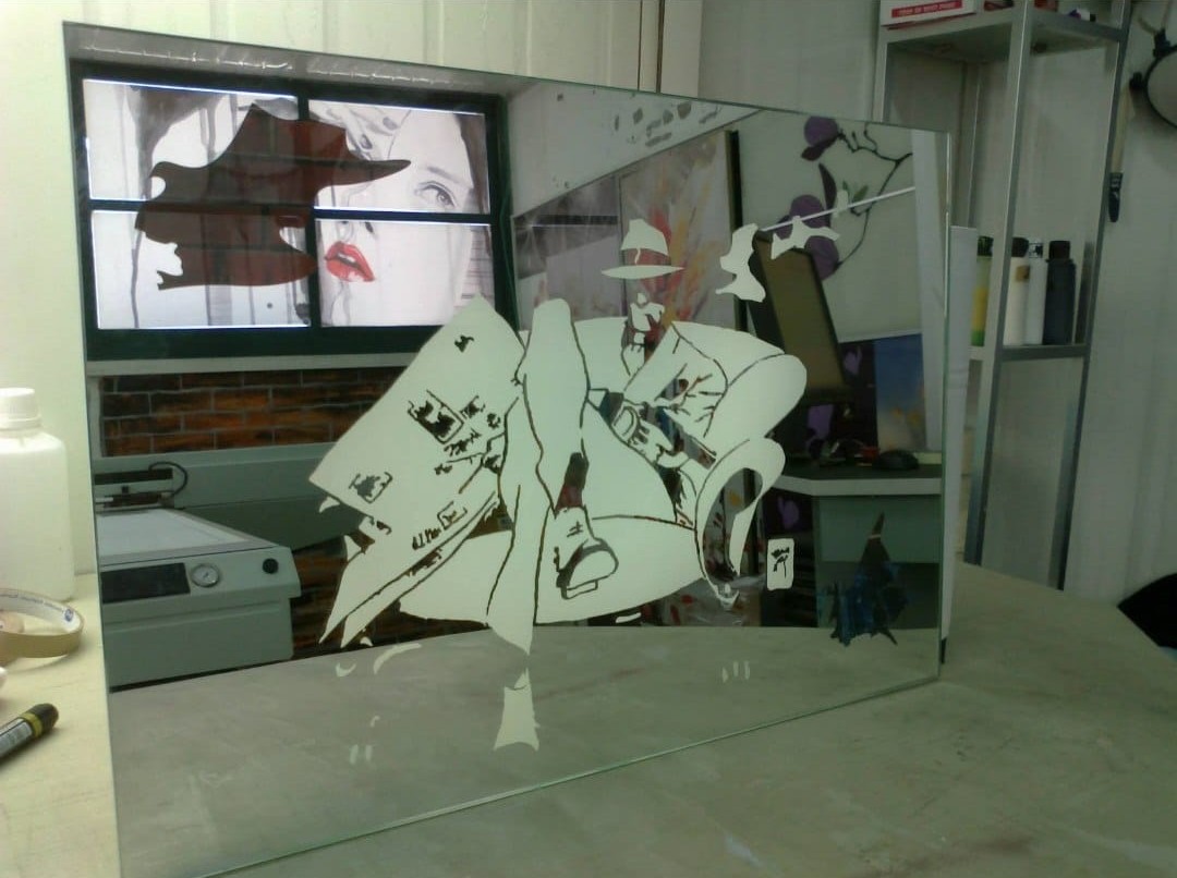A decorative mirror panel with stylized figures, displayed in the workshop.